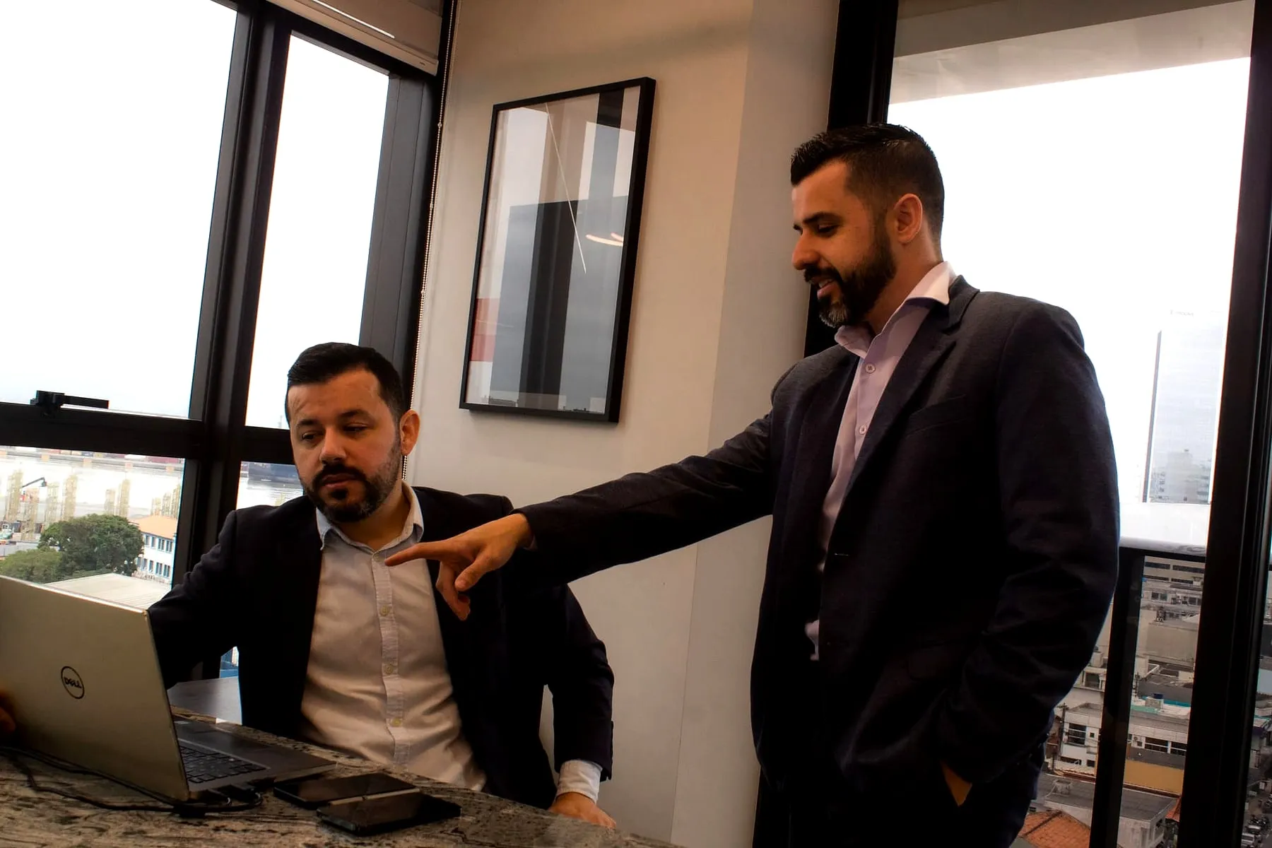 Os dois diretores da Regência Contabilidade no escritório, em conversa de trabalho, com o porto visível pela janela ao fundo.